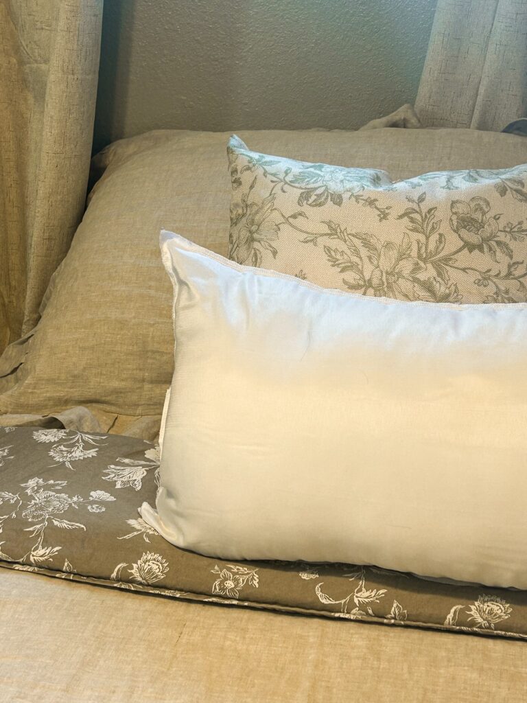 Layered linen pillows with sage green floral print on a cozy farmhouse bed
