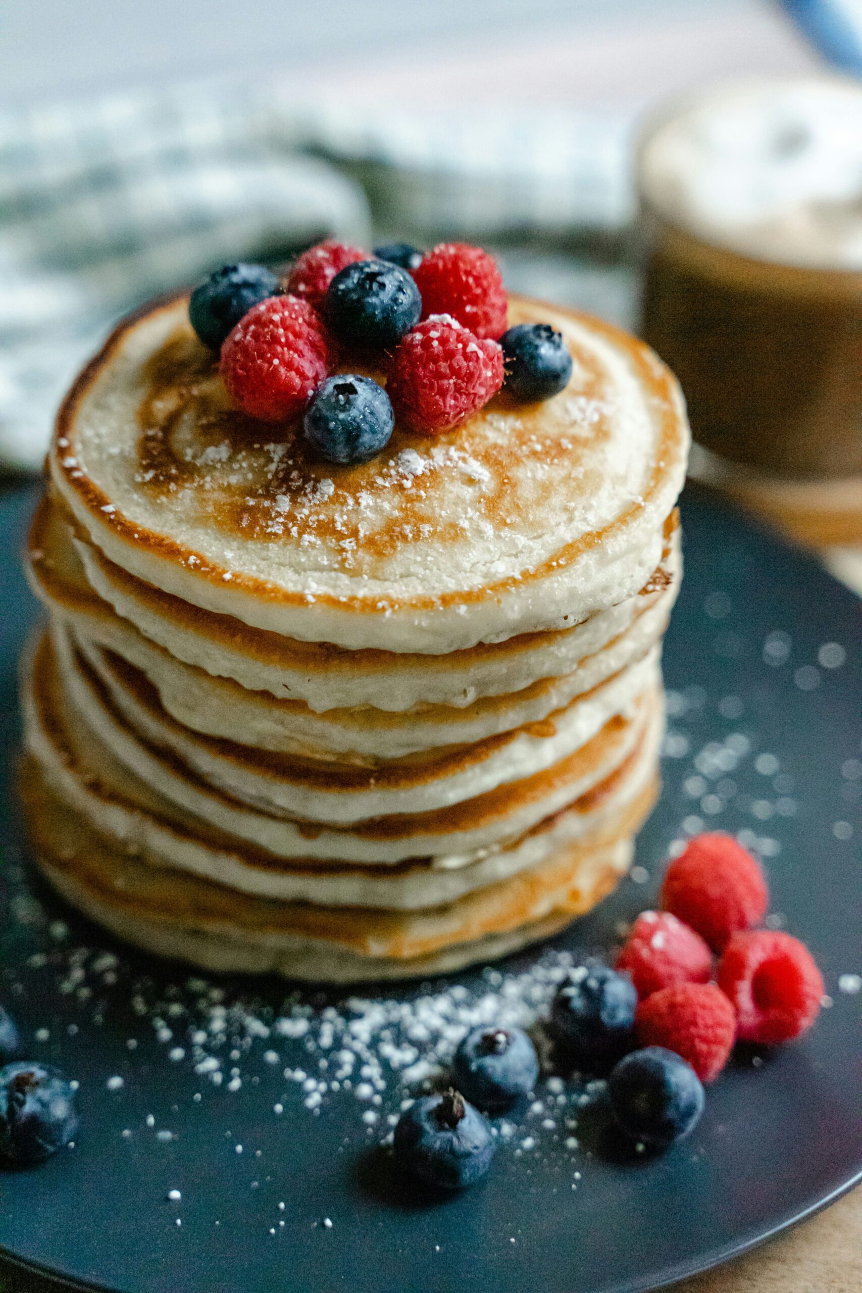 sourdough discard pancakes topped with raspberries and blueberries on a black plate