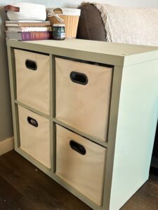 Sage green cube organizer with beige fabric bins beside a farmhouse sofa