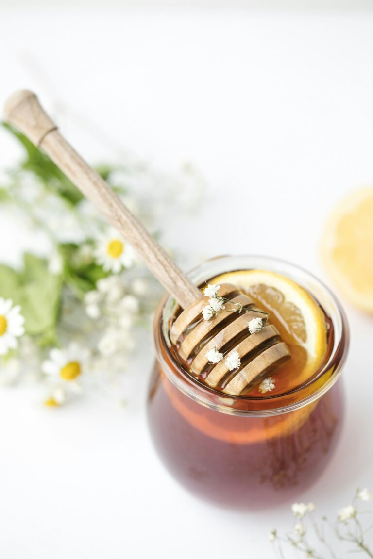 ar of raw honey with lemon slices and a wooden dipper, styled with chamomile flowers, representing fermented garlic honey ingredients